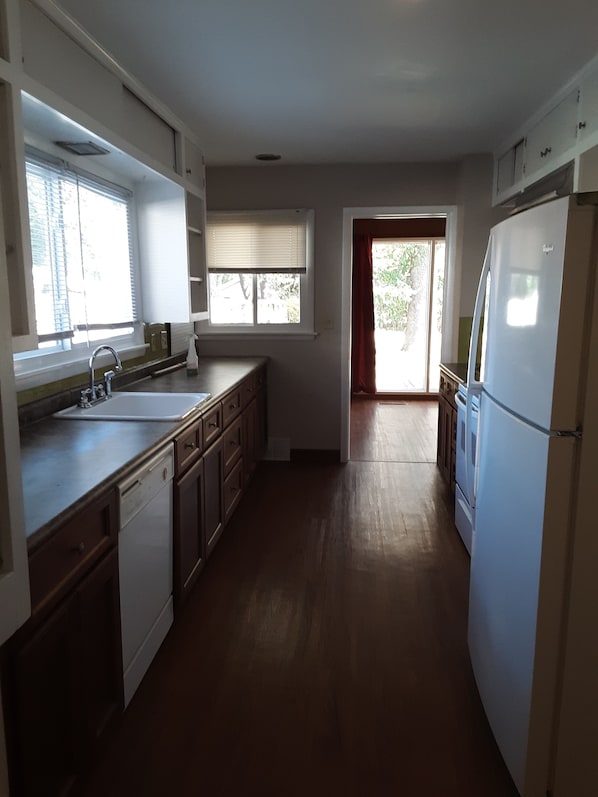 A kitchen with a dishwasher, sink, and refrigerator. There are windows with blinds and a door leading to another room. - Come Spread Out at Yellow Maple on Kings (Springfield)
