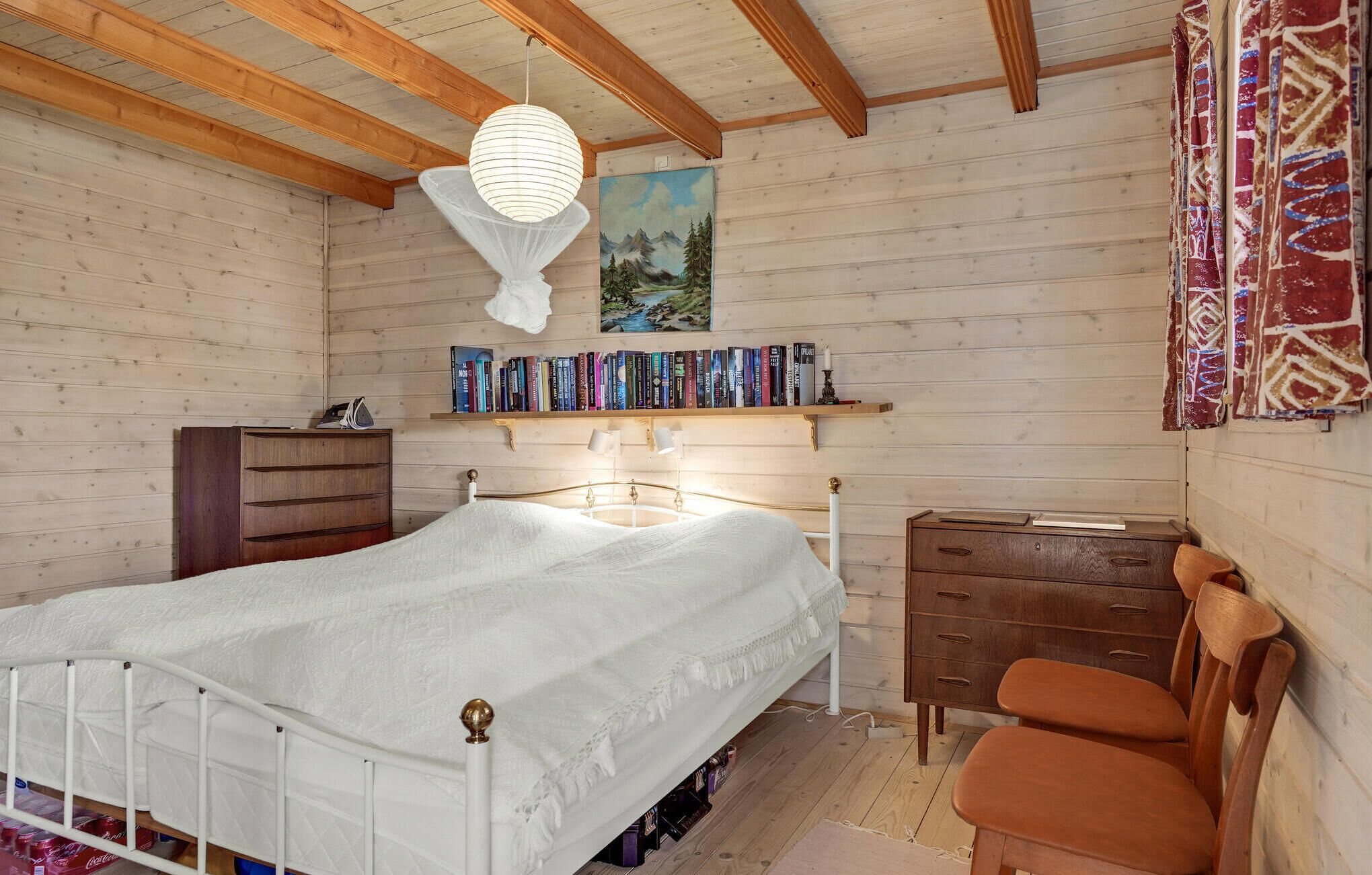 Een slaapkamer met een bed, een houten dressoir, boekenkasten en een schilderij.