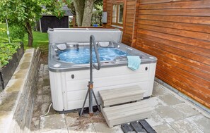 Relax in the hot tub with a seat, surrounded by a stone pathway and a small deck.