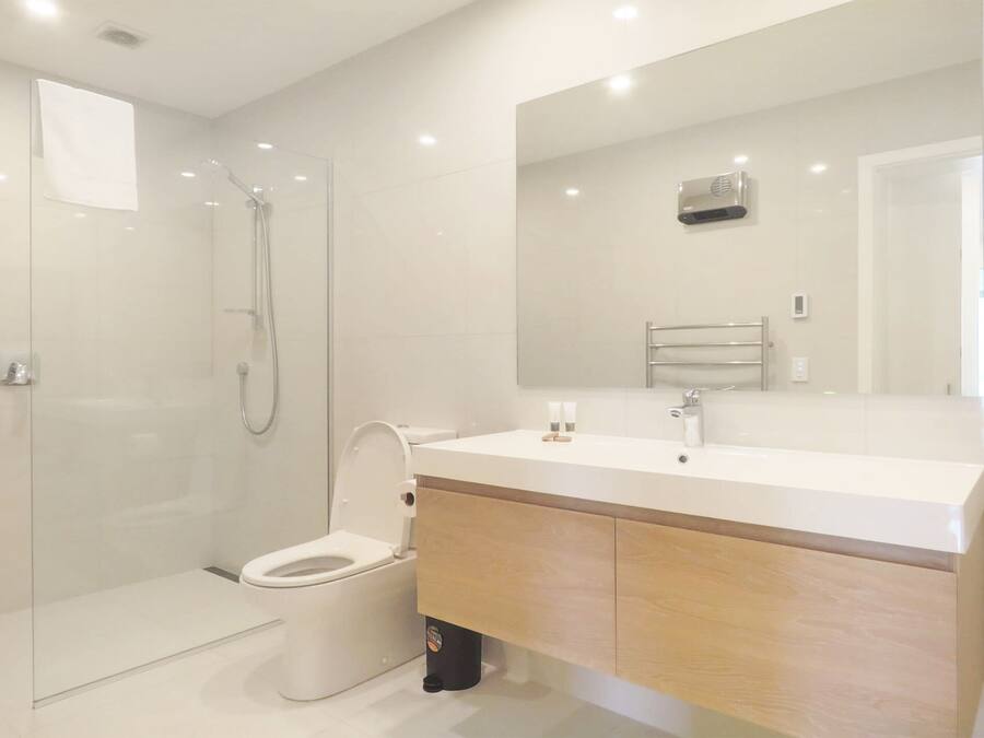 Un bagno moderno con doccia vetrata, un water bianco e un mobile vanitario in legno con uno specchio sopra.