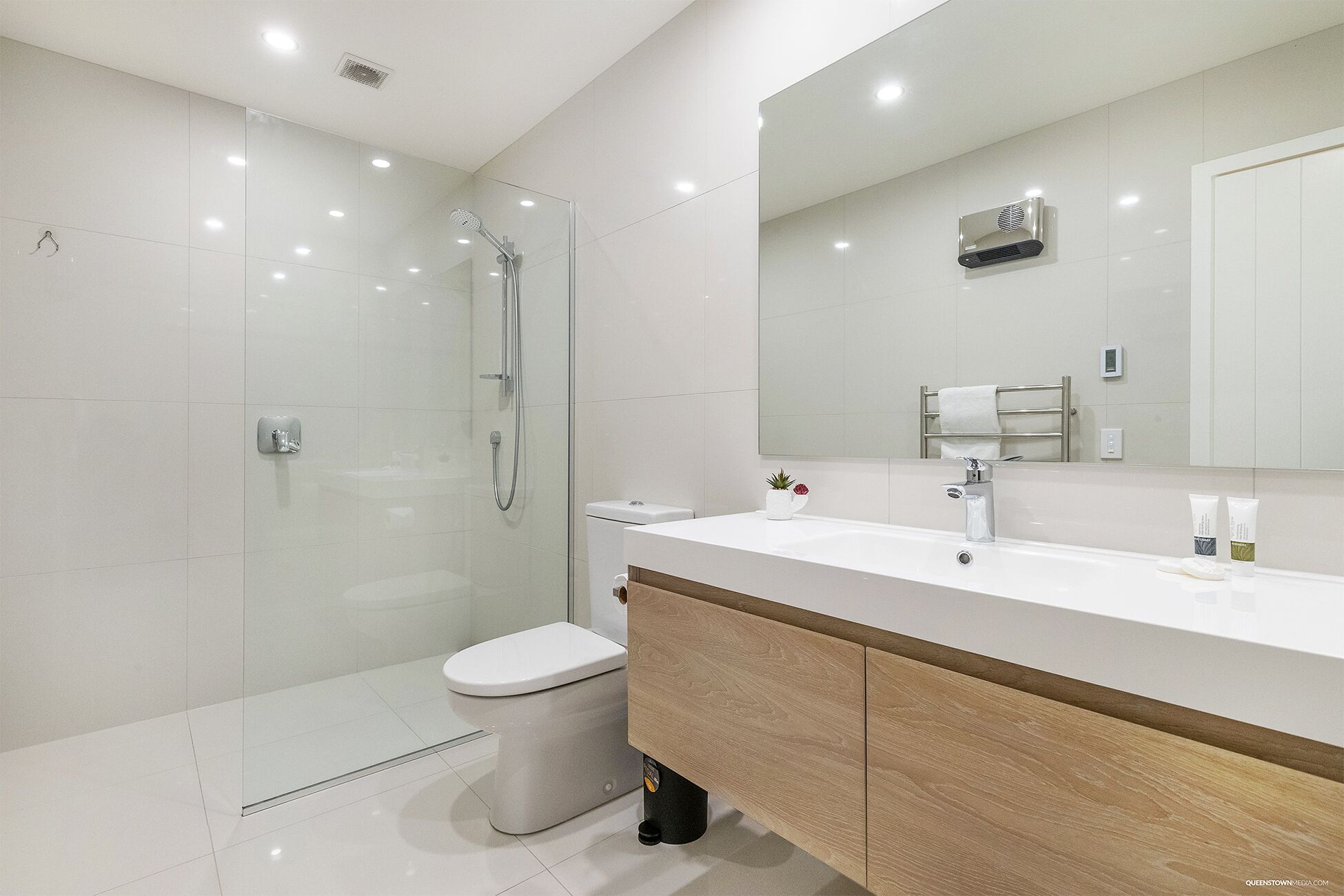 A modern bathroom with a glass shower enclosure, a white toilet, a vanity with a mirror, and a wooden cabinet.