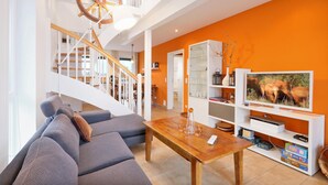 Un soggiorno moderno con una scala in legno, una televisione e una libreria.