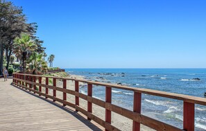 Una passerella in legno con ringhiera rossa che conduce a una spiaggia con palme e l'oceano.