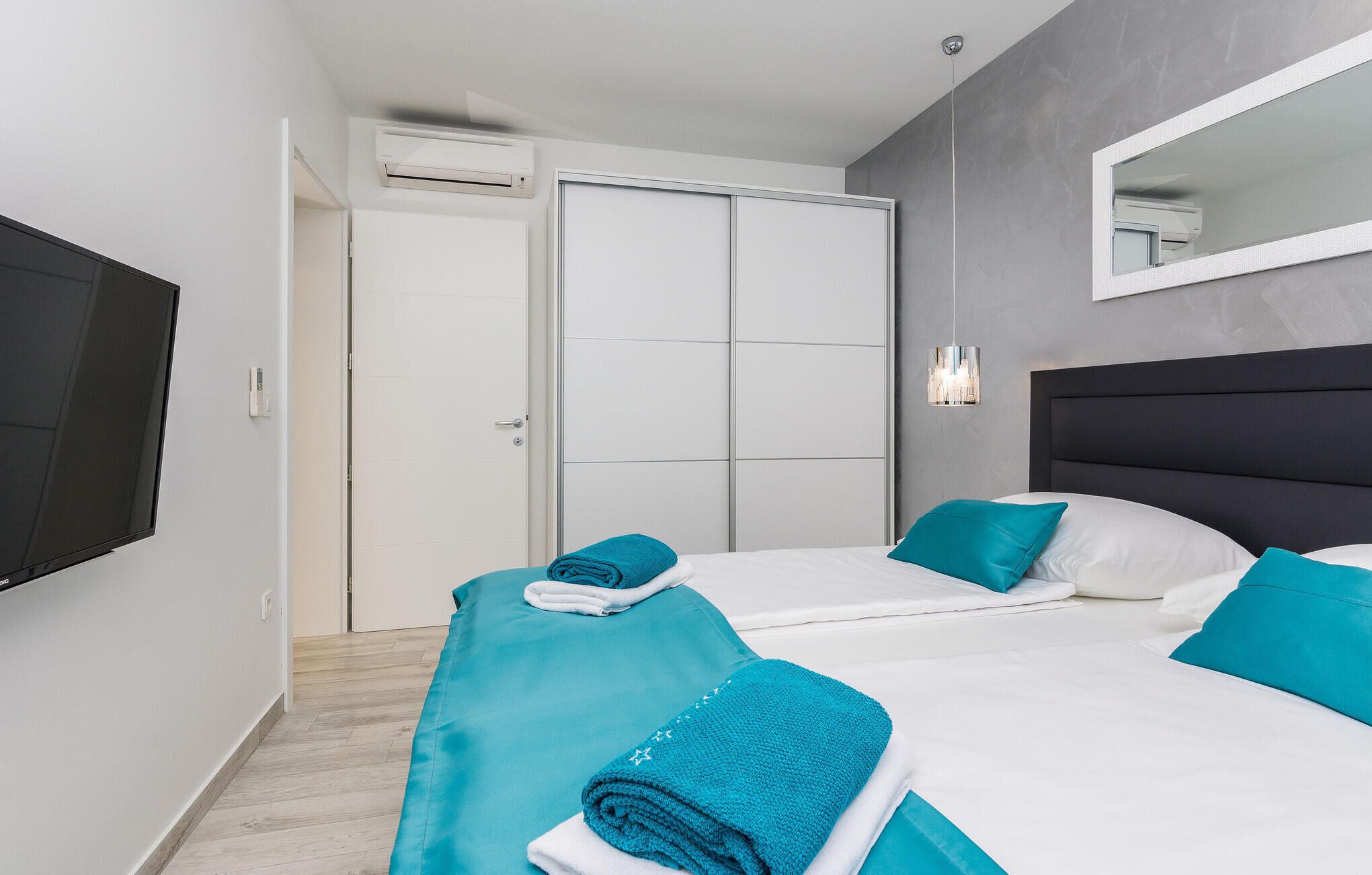A hotel room with two beds, a flat-screen TV, a mirror, and an air conditioning unit.