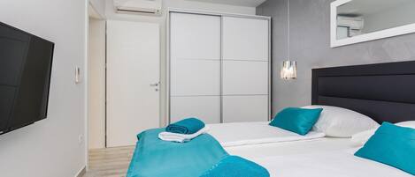 A hotel room with two beds, a flat-screen TV, a mirror, and an air conditioning unit.
