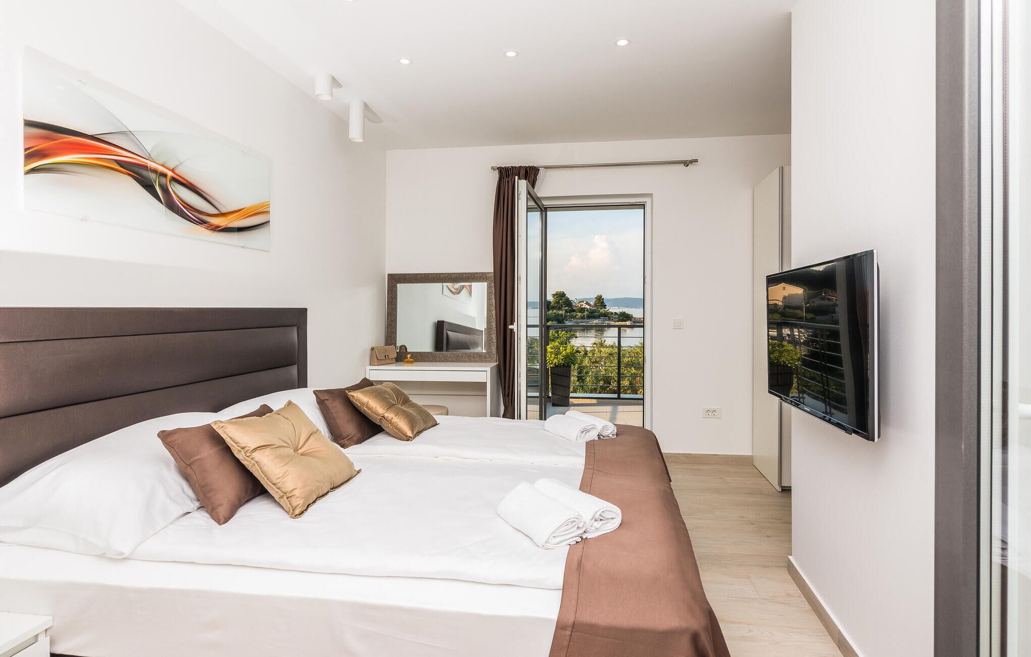 Ein modernes Hotelzimmer mit einem großen Bett, einem Flachbildfernseher und einem Balkon mit Blick auf das Wasser.