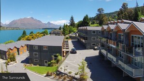 A modern hotel with multiple-story buildings, a parking area, and a view of a lake and mountains. - Alpine Village - 2 Bedroom Executive Apartment (Queenstown)