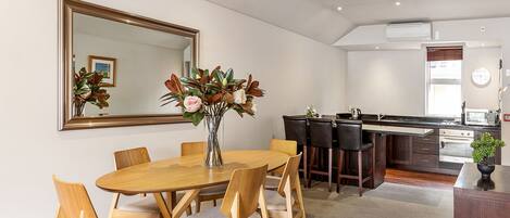 A modern kitchen with a central island, a dining area with a wooden table and chairs, and a large mirror on the wall.