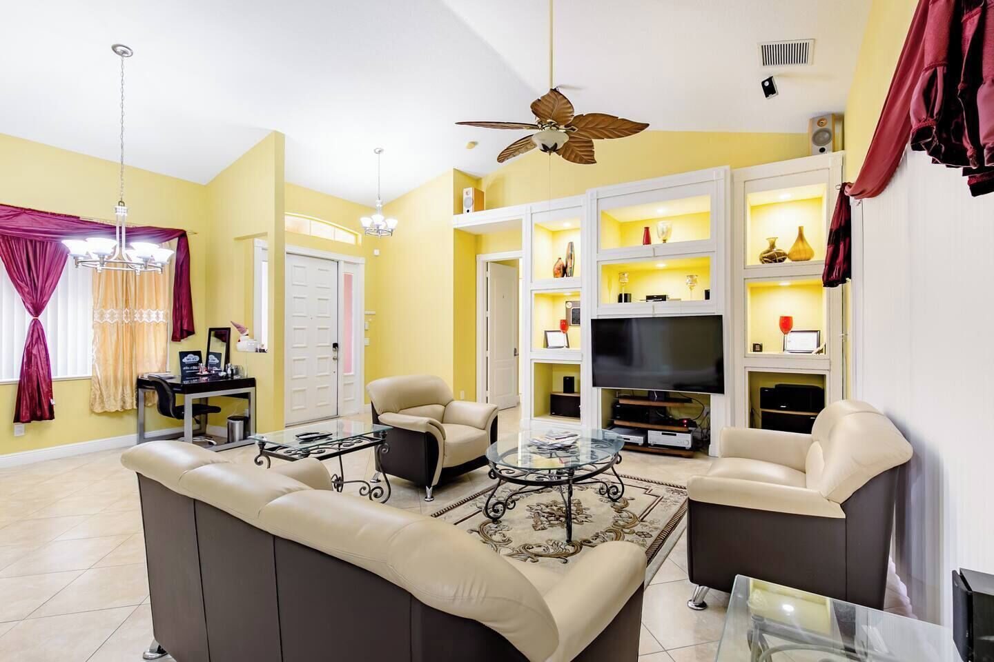 A living room with a sofa, armchairs, a coffee table, a TV, and a ceiling fan.