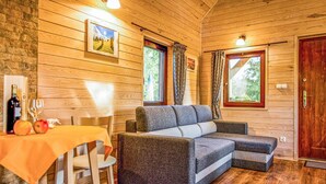 Una habitación acogedora con un sofá, una mesa de comedor con manzanas y una botella, y dos ventanas con cortinas.