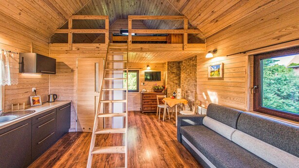 Interior acogedor de una cabaña con detalles de madera, un dormitorio en altillo, comedor y sofá.