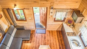 Una cabaña compacta con sofá, una pequeña cocina con lavamanos y una escalera que lleva a un espacio exterior.