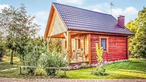 Una cabaña de troncos con porche, chimenea y un pequeño jardín.