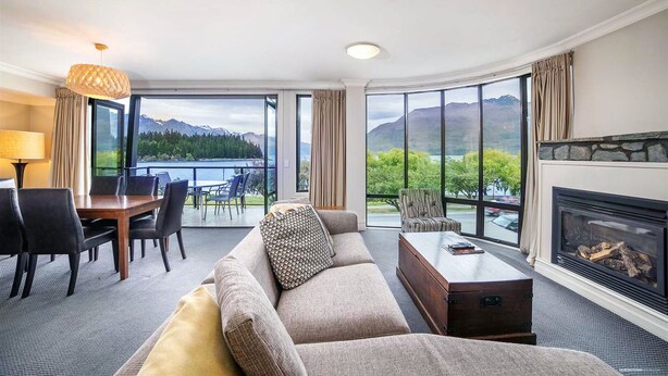 Habitación de hotel con un ventanal grande que ofrece una vista panorámica de montañas y un lago.