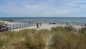 Ein Strand mit einer Holzpromenade, Personen, die am Ufer entlanggehen, und einer Flagge im Wasser.