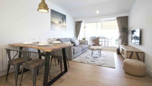 A modern living room with a dining area, a sofa, a TV, and a large window with curtains. - Atlantic | Rentals Collection (San Sebastián)