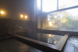 A hot spring area with stone steps leading into the water, a metal railing, and a view of trees through a large window. - Hanasansui (Kokonoe)