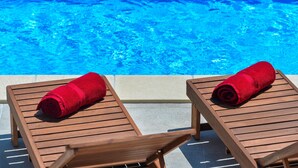 Two wooden lounge chairs with red towels, positioned by a pool with clear blue water. - Nice home in Varazdin Breg with sauna (Varazdin Breg)