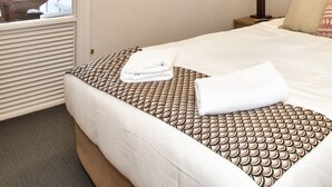 A hotel room with a bed, a nightstand, a lamp, and a window with curtains. - The Beacon - 2 Bedroom Town Center Apartment (Queenstown)
