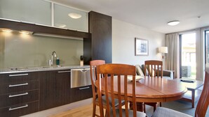 A modern kitchen with dark wooden cabinets, a stainless steel sink, and a dining area with a wooden table and chairs. - The Beacon - 2 Bedroom Town Center Apartment (Queenstown)