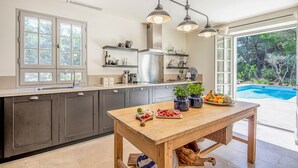 A modern kitchen with dark cabinets, a wooden table, and a view of a swimming pool. - Stunning home in Saint-Rémy-de-Provence (Saint-Rémy-de-Provence)
