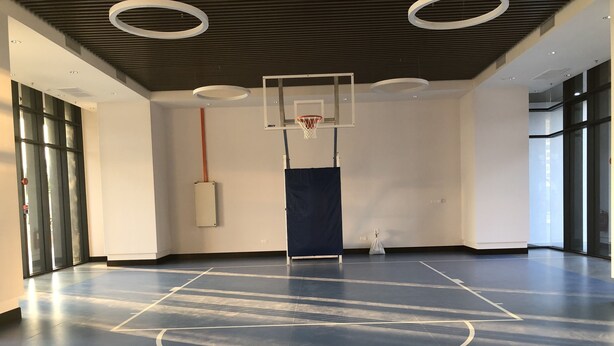 A basketball court with a hoop, a blue floor, and a white wall with a window. - Almas Suites By Iconic Bliss (Iskandar Puteri)