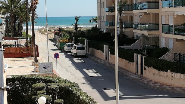 A coastal residential area with a street lined with palm trees and a view of the sea. - Les Dunes 2º Solo Familias! (Xeraco Playa)