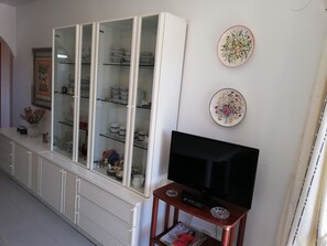 A living room with a glass-fronted cabinet containing dishes and a flat-screen TV on a wooden stand.