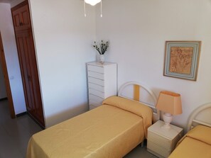 A bedroom with two beds, a dresser, a nightstand, a lamp, a framed picture, and a door.