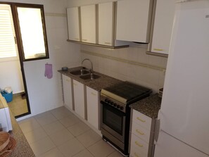 A kitchen with white cabinets, a granite countertop, a stainless steel sink, and an oven. - Les Dunes 2º Solo Familias! (Xeraco Playa)