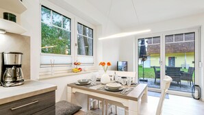 A modern kitchen with a coffee maker, dining table, chairs, and a view of the outdoors. - Reetdachhaus Waldidylle (Zirchow/Usedom)