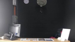 Ein Zimmer mit Schreibtisch, Computer, einer Uhr und einer Pendelleuchte.