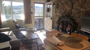 A cozy living room with a stone fireplace, a large window with curtains, a sofa, a coffee table, and a television. - Peaceful cozy place on the river with great views (Winter Park)
