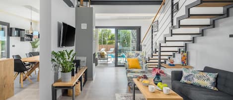 Una sala de estar moderna con una escalera, un comedor y vistas al exterior.