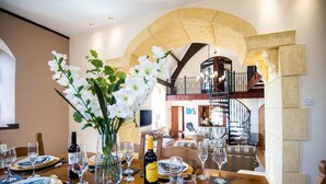 A dining area with a table set for a meal, a bottle of champagne, and a vase of white flowers. - Unique historic school‑house conversion with log burner (Laugharne (2.8miles W))