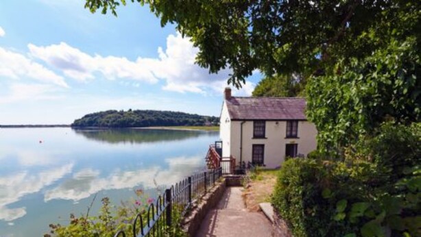 A white building with a paved pathway leading to it, surrounded by greenery and a calm body of water. - Unique historic school‑house conversion with log burner (Laugharne (2.8miles W))