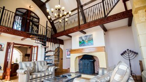 A spacious living room with a fireplace, a staircase, and a chandelier. - Unique historic school‑house conversion with log burner (Laugharne (2.8miles W))
