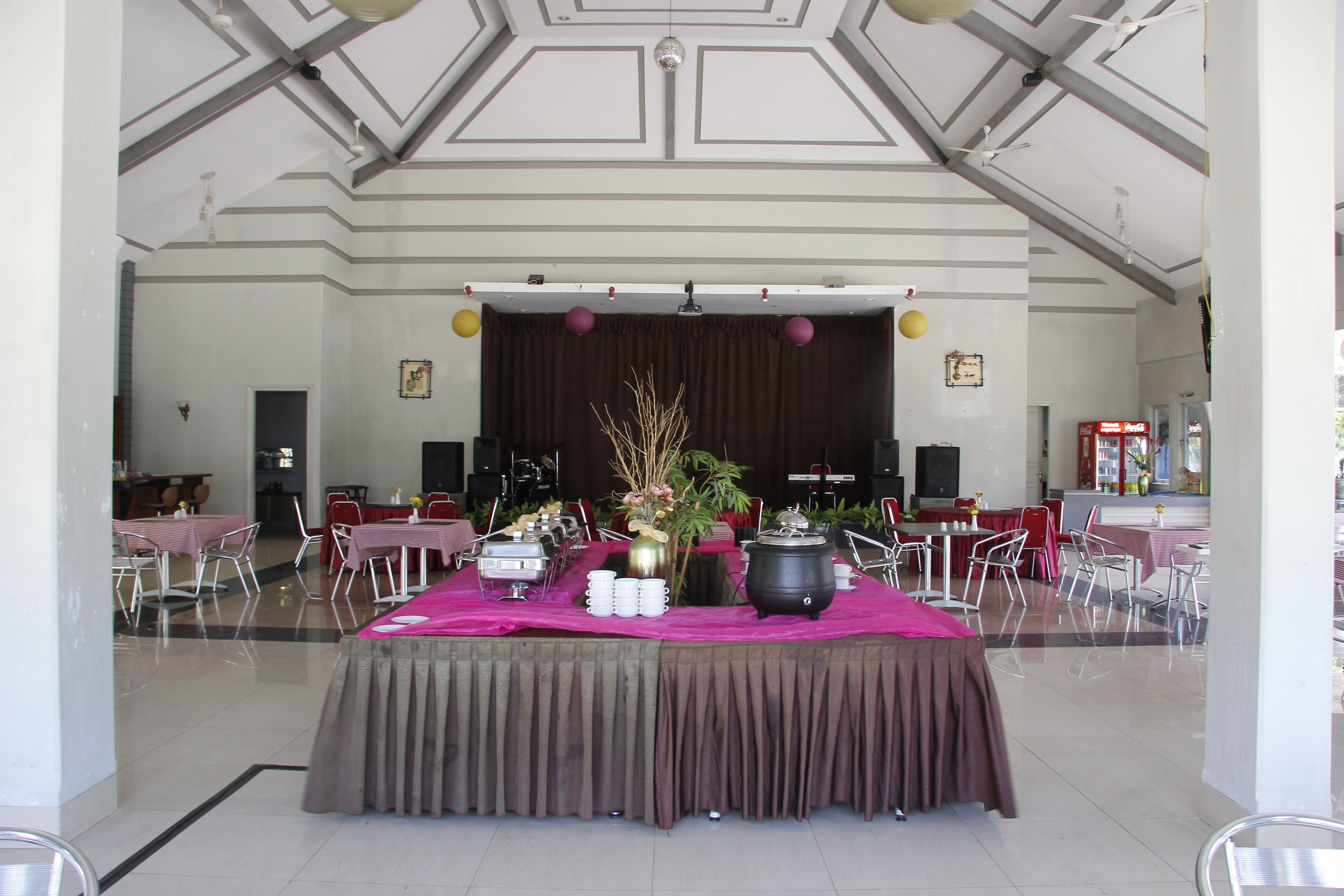 A banquet hall with a stage, tables with pink tablecloths, and a buffet setup.