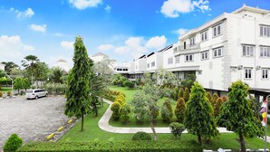 Un immeuble moderne à plusieurs étages, doté d’un jardin bien entretenu et d’une allée pavée.