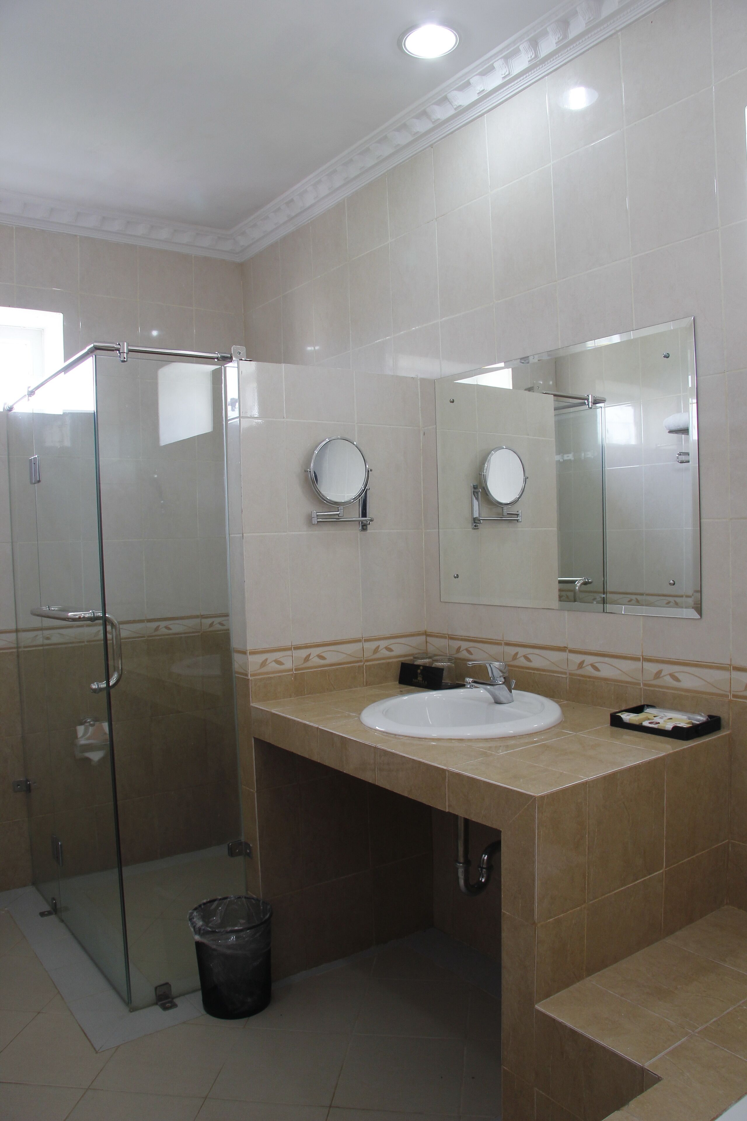 Un baño moderno con cabina de ducha de vidrio, un lavabo con espejo y un cubo de basura.