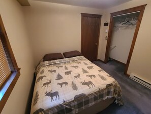 Een slaapkamer met een bed, een kast met kapstok en een deur.