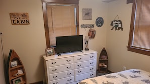 Un dormitorio con cama, cómoda, televisión y varias decoraciones en la pared.