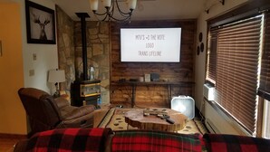 Una sala de estar acogedora con chimenea de piedra, un sofá cómodo, una mesa de centro de madera y un televisor montado en la pared.