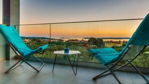 A balcony with two turquoise chairs and a small table, overlooking a scenic view of a town and water during sunset. - Amazing home in Fazana (Fazana)