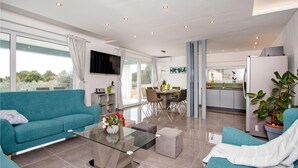 A modern living room with a teal sofa, a glass coffee table, and a dining area with a table and chairs. - Amazing home in Fazana (Fazana)