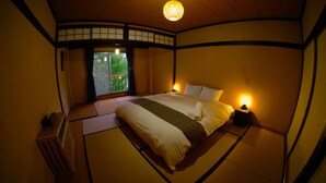 Ett traditionellt japanskt sovrum med tatamimattor på golvet, en låg säng och en skjutdörr som leder ut till en balkong.
