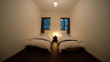 A small, dimly lit room with two beds, a nightstand, and two windows with curtains.
