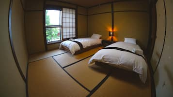 A traditional Japanese room with tatami flooring, two beds, a window with shoji screens, and a bedside lamp.