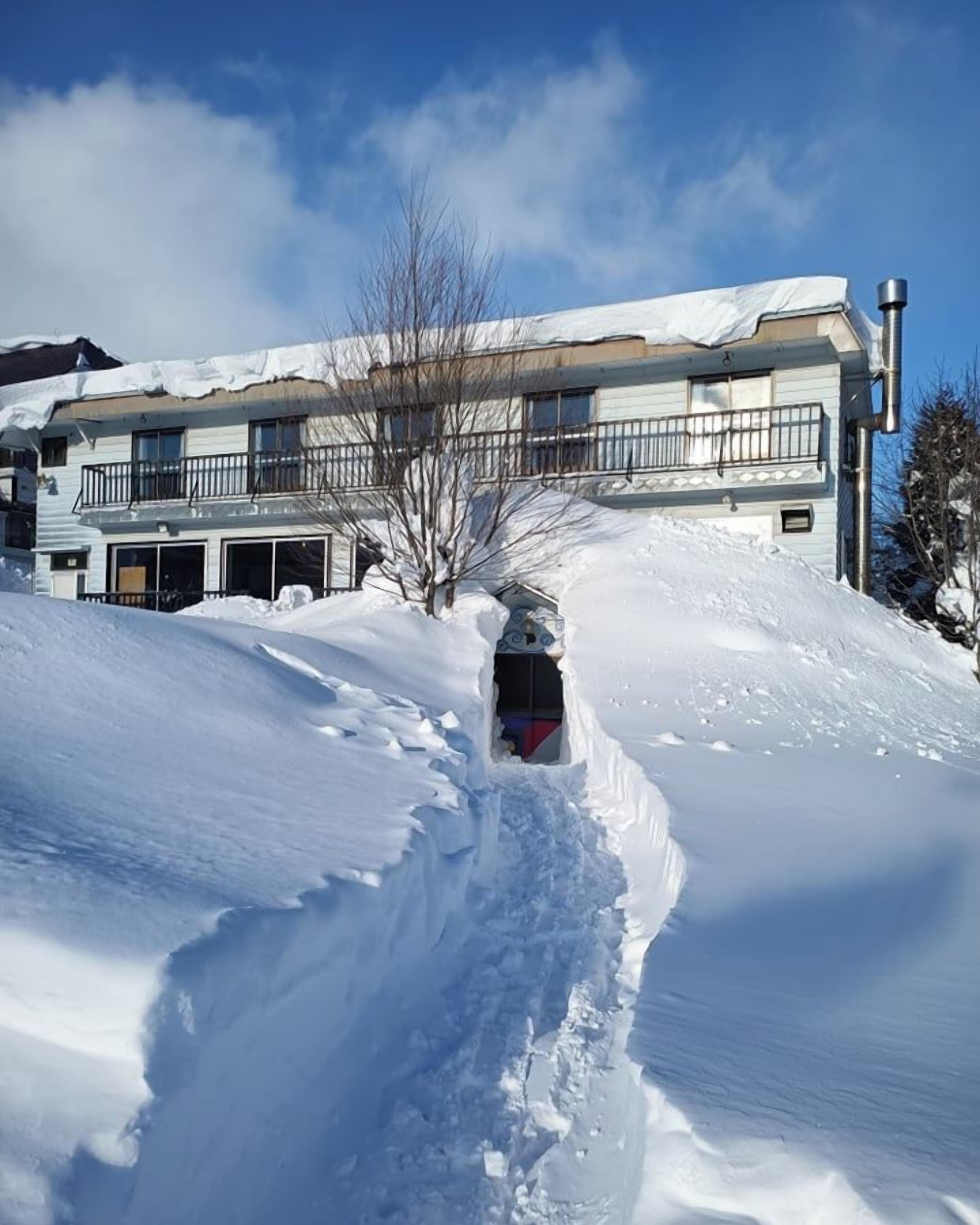 A snow-covered path leading to a building with a balcony and a garage.