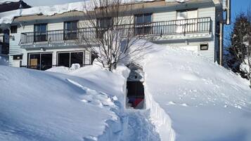 A snow-covered path leading to a building with a balcony and a garage.